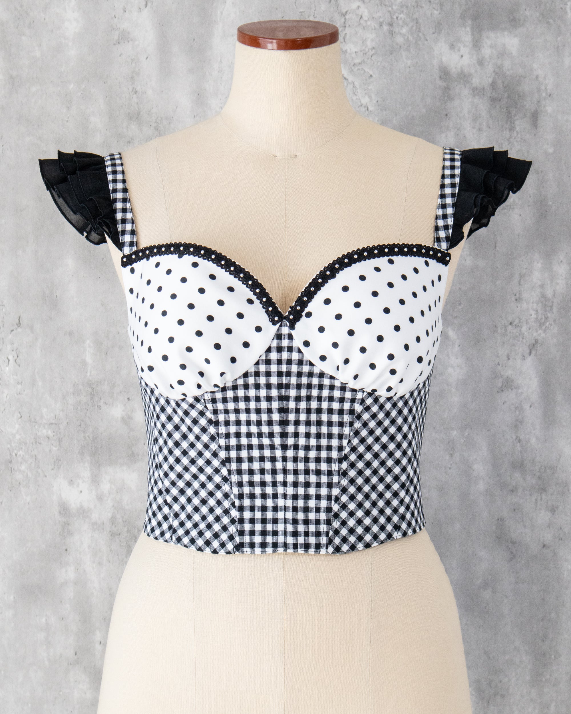 水玉とギンガム柄を組み合わせたビスチェ。肩に黒のフリル、胸元にはスタッズブレードのアクセント。