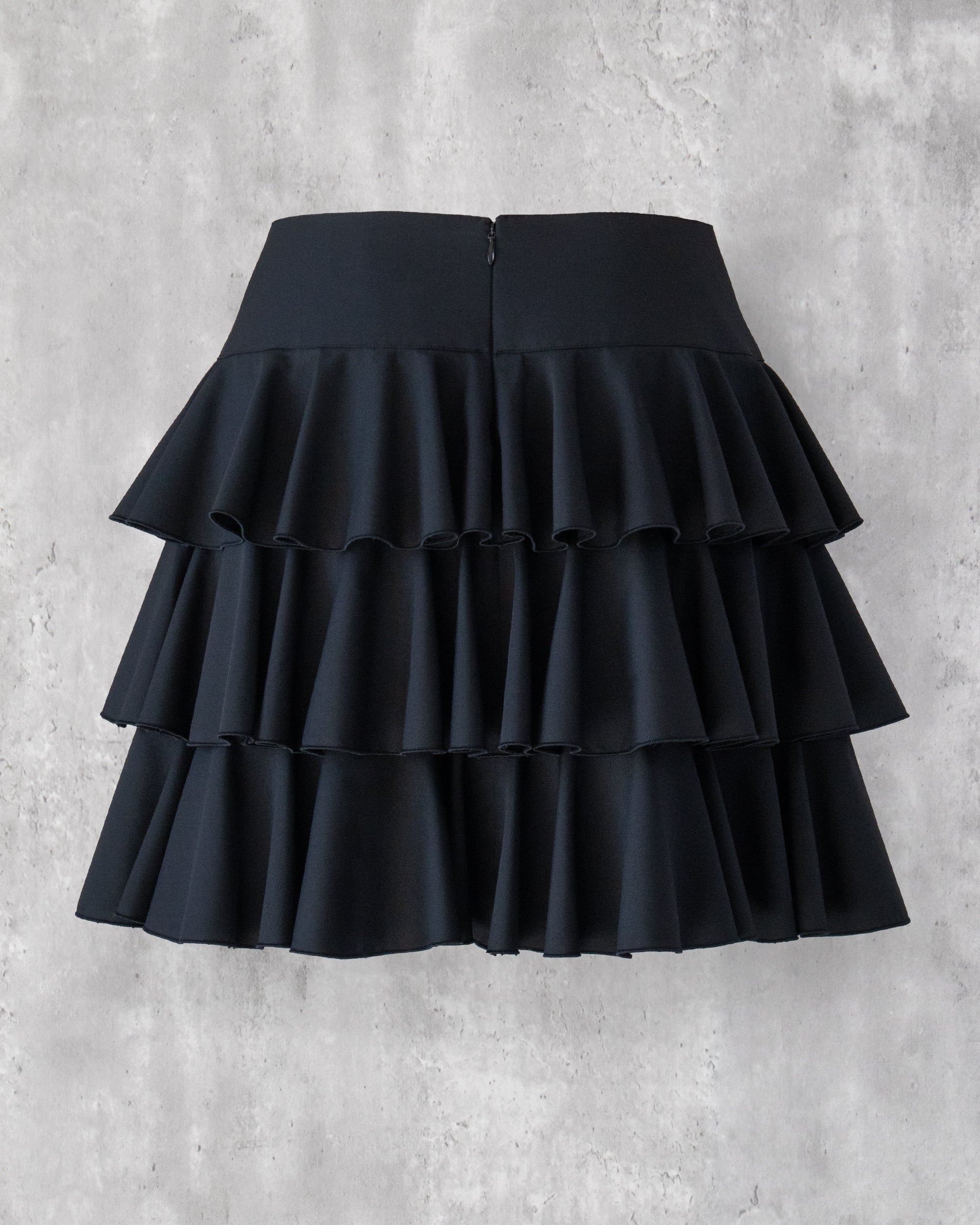 黒の３段ティアードフリルスカートのバックスタイル。コンシールファスナーあき。膝上丈。上品な光沢に肌触りの良い生地。