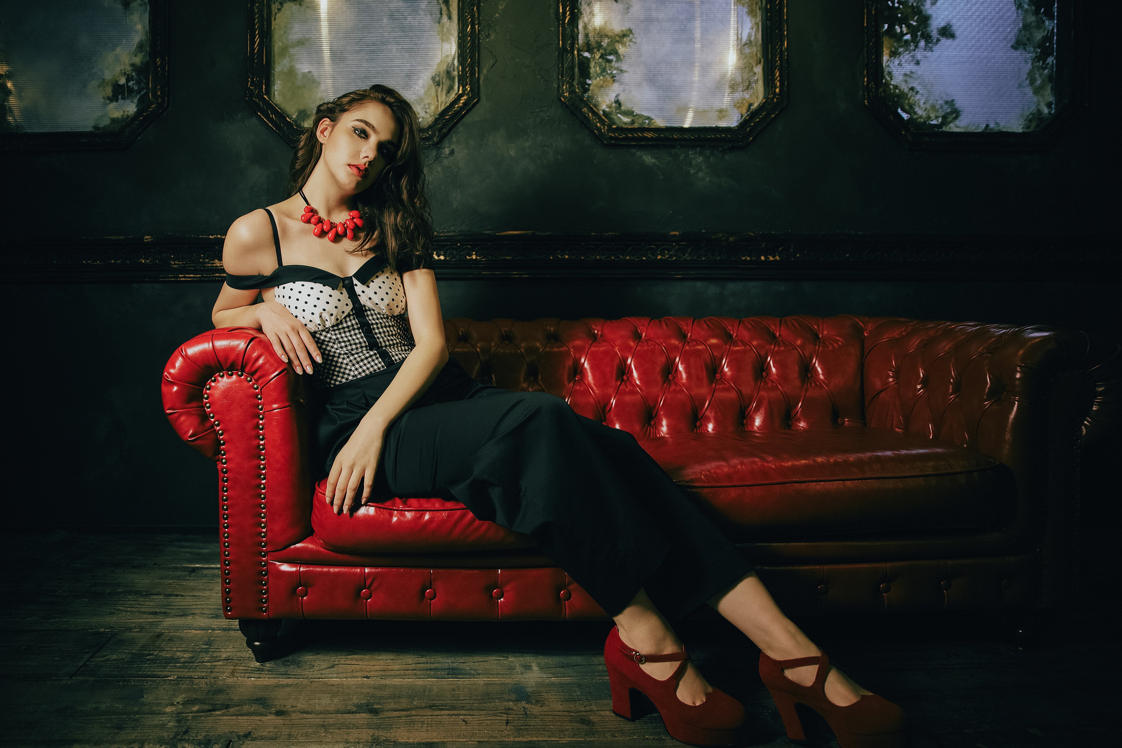 Woman in designer bustier and wide leg trousers seated on a red leather sofa in a dark atmospheric interior — Atë small-batch fashion label Tokyo